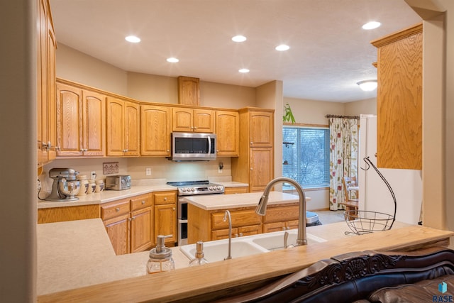 kitchen featuring stainless steel appliances, recessed lighting, light countertops, a sink, and a peninsula