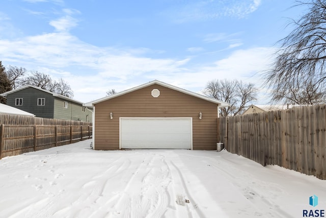 snow covered garage with a detached garage and fence