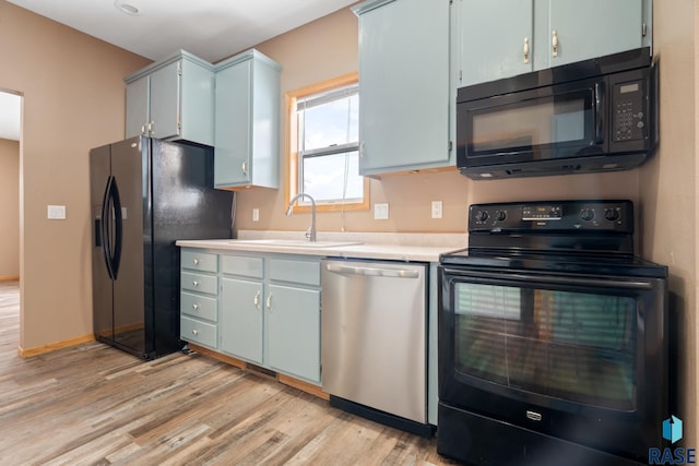 kitchen with baseboards, light wood-style flooring, light countertops, black appliances, and a sink