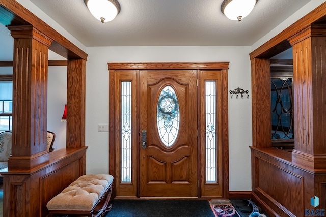 foyer entrance with a textured ceiling, dark carpet, and decorative columns