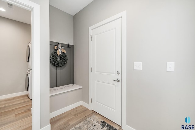 mudroom with light wood-style flooring, visible vents, baseboards, and stacked washer / dryer