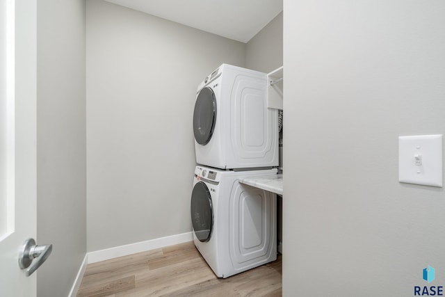 clothes washing area featuring laundry area, light wood finished floors, stacked washer / dryer, and baseboards