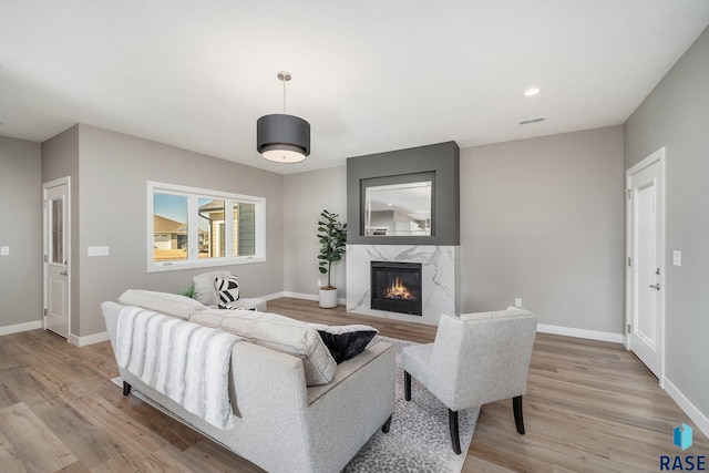 living area with light wood-style flooring, a fireplace, visible vents, and baseboards