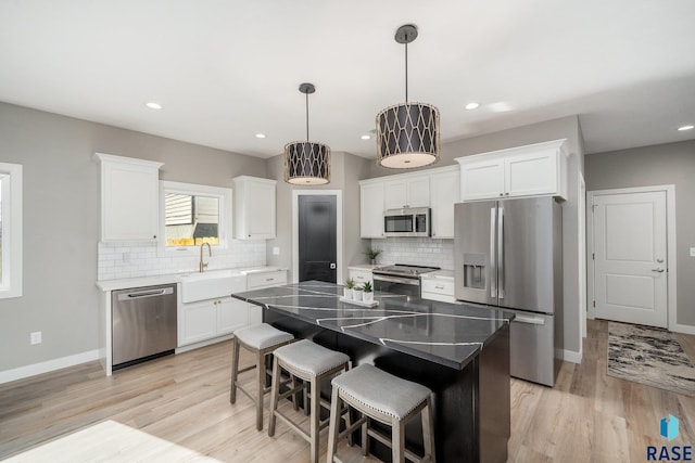 kitchen with light wood-style flooring, stainless steel appliances, white cabinetry, a center island, and decorative light fixtures