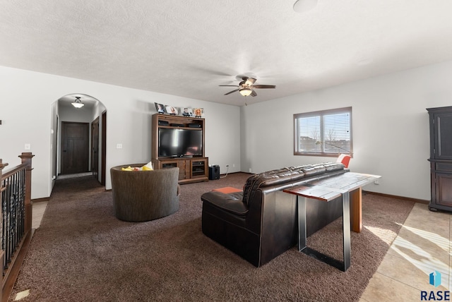 carpeted living area featuring arched walkways, ceiling fan, a textured ceiling, and baseboards