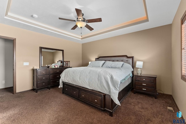 bedroom featuring dark colored carpet, a raised ceiling, and a ceiling fan