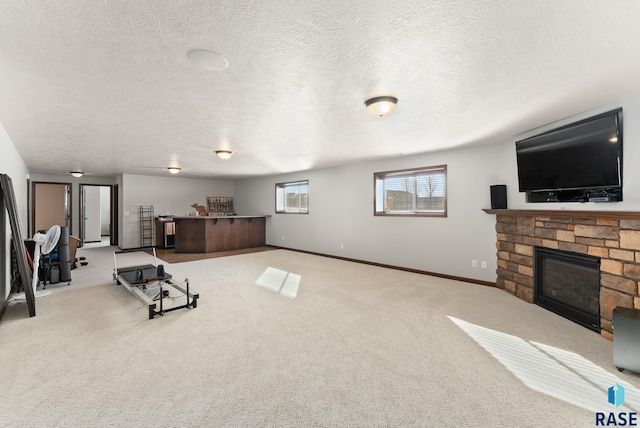 workout room featuring light carpet, a stone fireplace, a textured ceiling, and baseboards