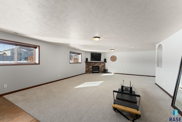 living room featuring a textured ceiling, light colored carpet, a fireplace, visible vents, and baseboards