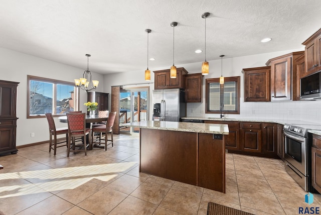 kitchen featuring dark brown cabinetry, appliances with stainless steel finishes, light stone counters, a center island, and decorative light fixtures