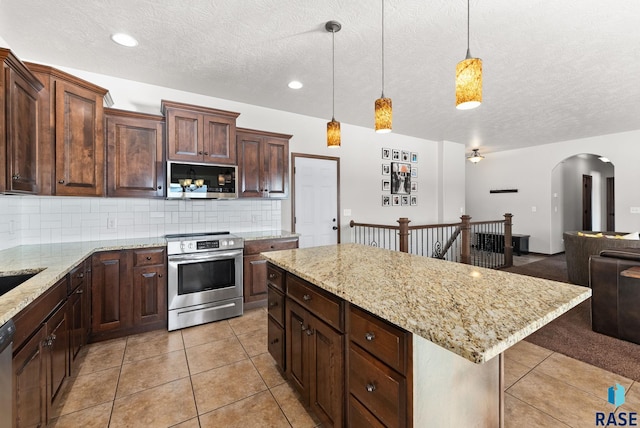 kitchen with a kitchen island, open floor plan, decorative light fixtures, stainless steel appliances, and backsplash