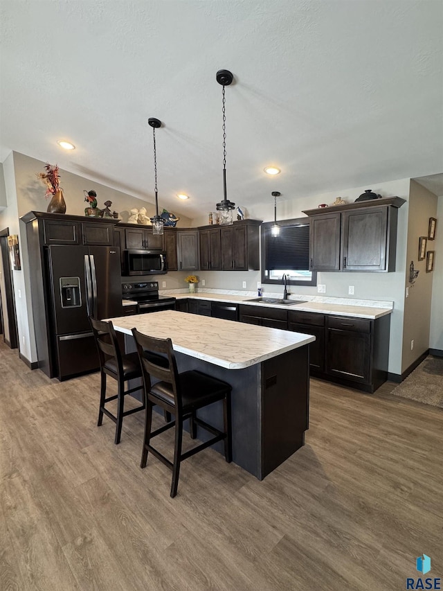 kitchen featuring dark brown cabinetry, appliances with stainless steel finishes, a center island, hanging light fixtures, and a sink