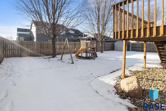 snowy yard featuring a storage unit, a playground, a fenced backyard, and an outdoor structure