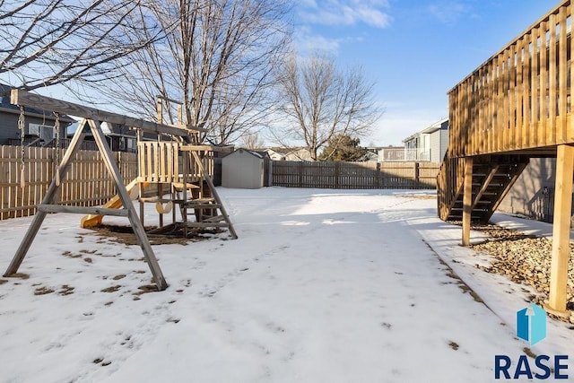 yard covered in snow featuring a storage shed, a playground, a fenced backyard, and an outdoor structure