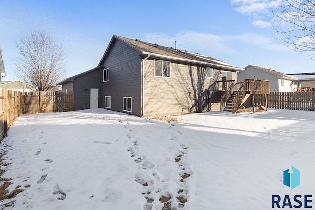 snow covered back of property with fence, stairway, and a wooden deck