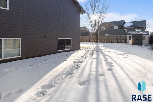 view of snow covered exterior featuring a storage unit, an outdoor structure, and fence