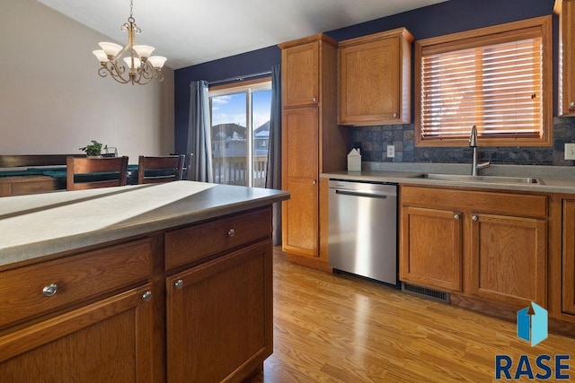 kitchen with brown cabinets, decorative light fixtures, stainless steel dishwasher, a sink, and light wood-type flooring