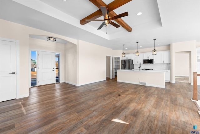 unfurnished living room featuring baseboards, visible vents, arched walkways, dark wood-type flooring, and a tray ceiling