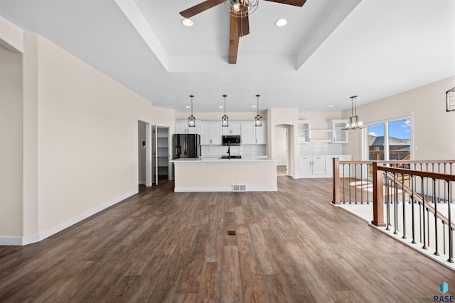 unfurnished living room with recessed lighting, baseboards, wood finished floors, a tray ceiling, and ceiling fan with notable chandelier