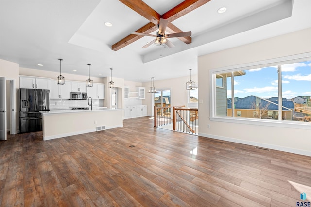 kitchen featuring white cabinets, light countertops, black fridge, stainless steel microwave, and decorative light fixtures