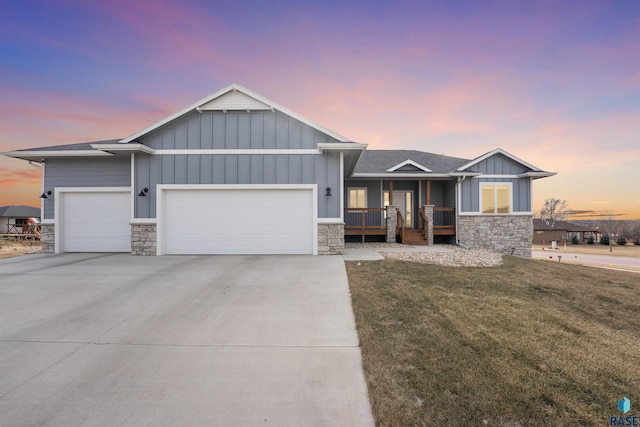 view of front of home with a yard, covered porch, board and batten siding, a garage, and stone siding