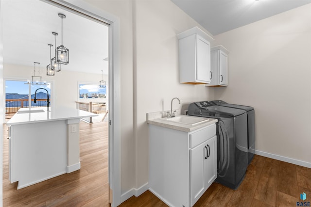 laundry area with washer and dryer, cabinet space, a sink, and wood finished floors