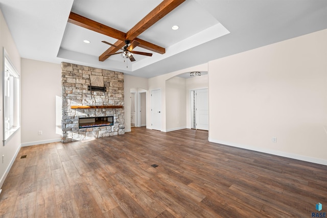 unfurnished living room featuring a fireplace, a ceiling fan, baseboards, beam ceiling, and dark wood-style floors