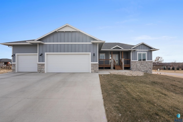 view of front facade featuring a porch, a garage, stone siding, board and batten siding, and a front yard