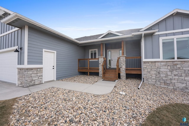 doorway to property with a garage, stone siding, a porch, and board and batten siding