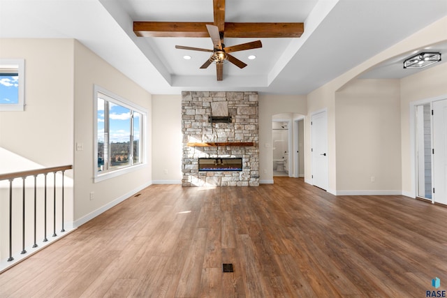 unfurnished living room featuring a stone fireplace, beamed ceiling, wood finished floors, and baseboards