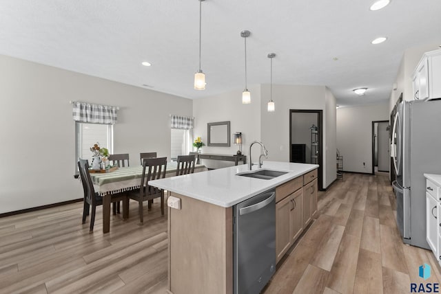 kitchen featuring decorative light fixtures, stainless steel appliances, white cabinets, a sink, and an island with sink