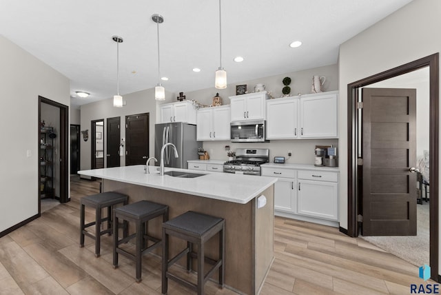 kitchen featuring a kitchen island with sink, stainless steel appliances, a sink, light countertops, and pendant lighting