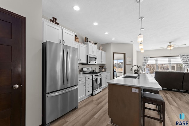 kitchen featuring appliances with stainless steel finishes, hanging light fixtures, light countertops, white cabinetry, and a sink