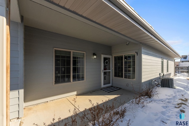 snow covered property entrance with central AC unit and a patio