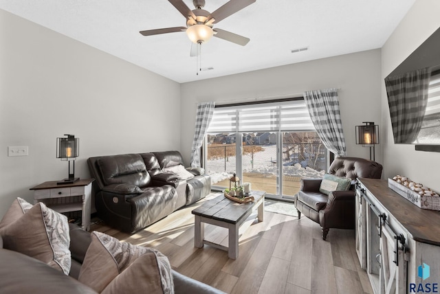 living room featuring light wood-style floors, visible vents, and ceiling fan