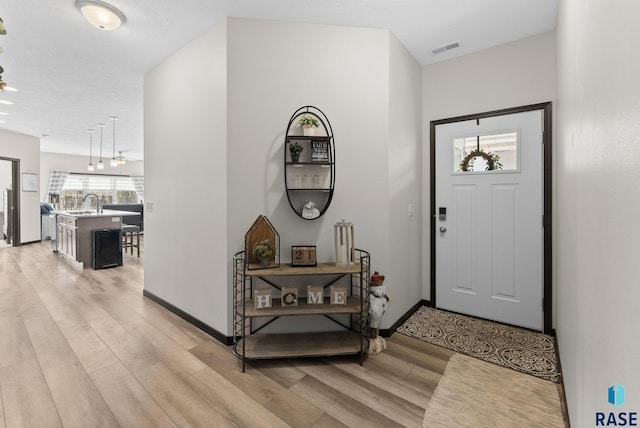 foyer with light wood-type flooring, visible vents, and baseboards