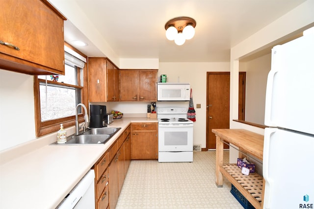 kitchen featuring light floors, light countertops, brown cabinetry, a sink, and white appliances