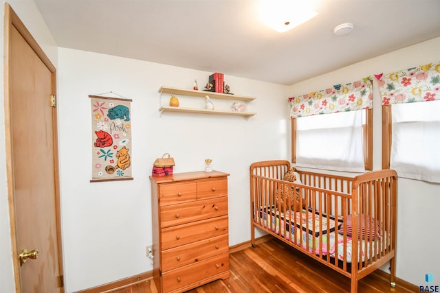 bedroom with a crib, baseboards, and dark wood finished floors