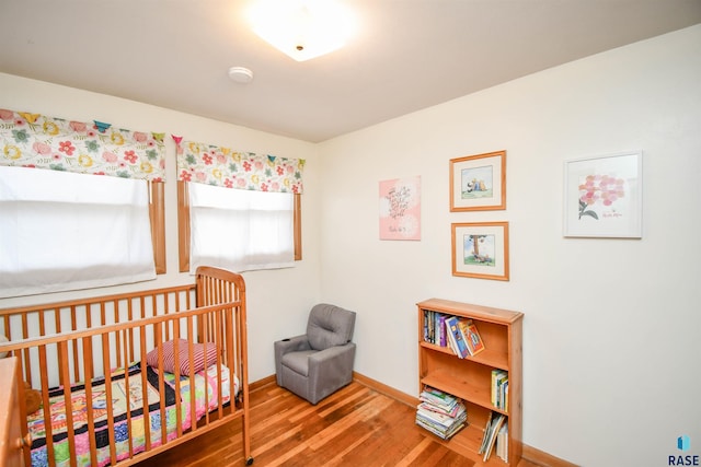 bedroom with a nursery area, wood finished floors, and baseboards