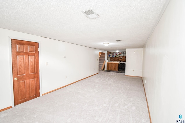 unfurnished living room with light carpet, stairway, a textured ceiling, and visible vents