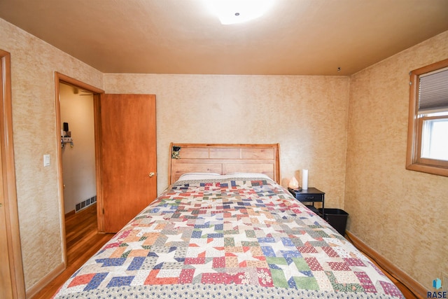 bedroom with dark wood-type flooring, visible vents, and wallpapered walls