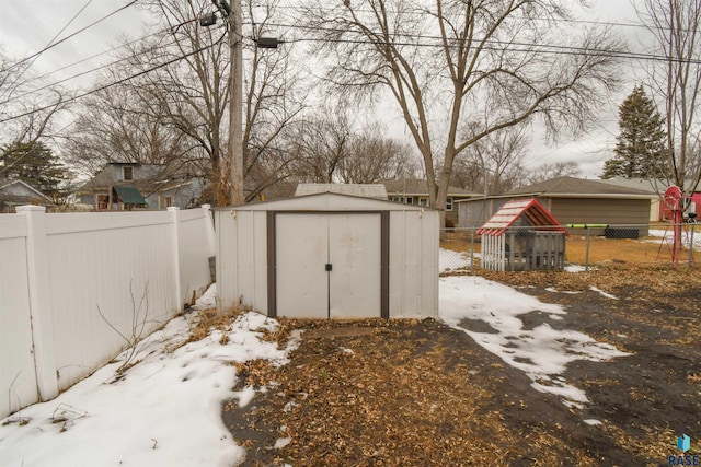 snow covered structure with an outbuilding, a shed, and a fenced backyard