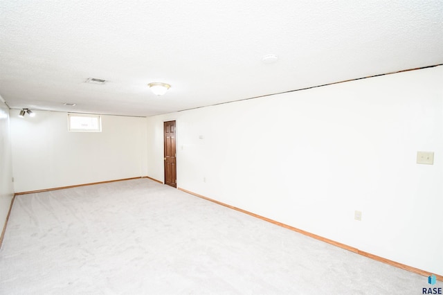 below grade area with a textured ceiling, carpet, visible vents, and baseboards