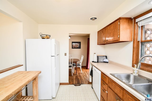 kitchen with white appliances, brown cabinets, light countertops, light floors, and a sink