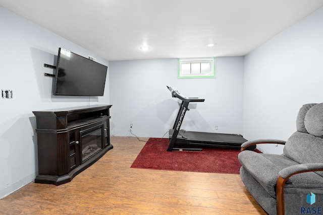 workout area featuring recessed lighting, light wood-style flooring, and a glass covered fireplace