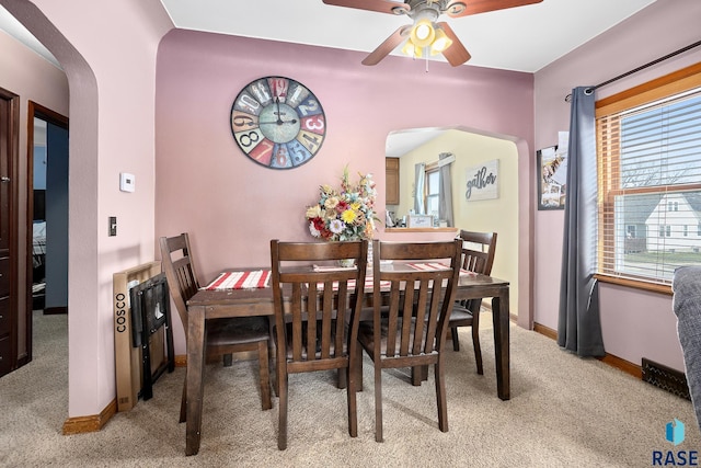 dining space with baseboards, arched walkways, a ceiling fan, and light colored carpet