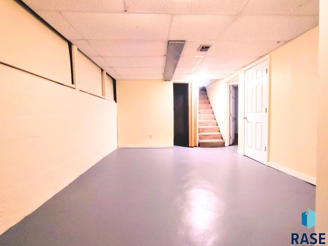 finished basement featuring a paneled ceiling, stairway, visible vents, and baseboards