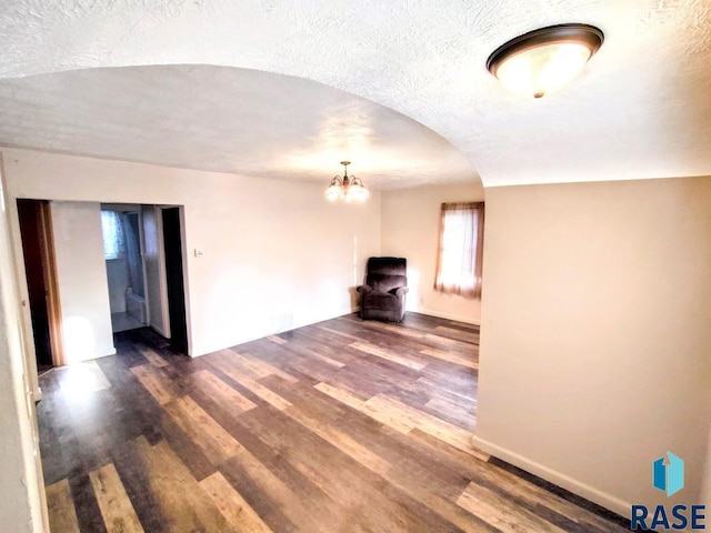 empty room featuring arched walkways, a textured ceiling, a chandelier, wood finished floors, and baseboards