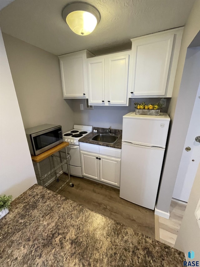 kitchen featuring dark countertops, white appliances, white cabinetry, and a sink