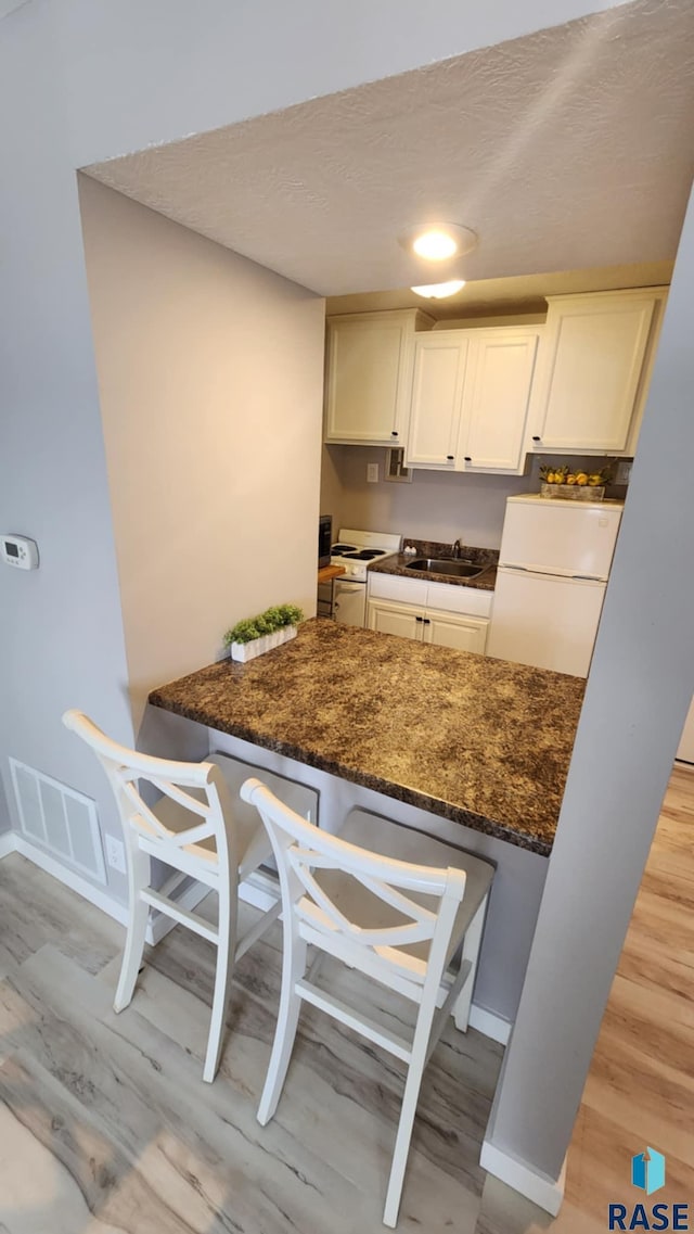 kitchen with visible vents, white cabinets, a sink, dark stone countertops, and white appliances