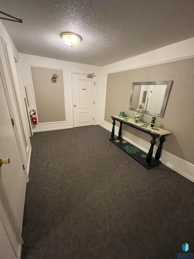 hall with baseboards, dark colored carpet, and a textured ceiling